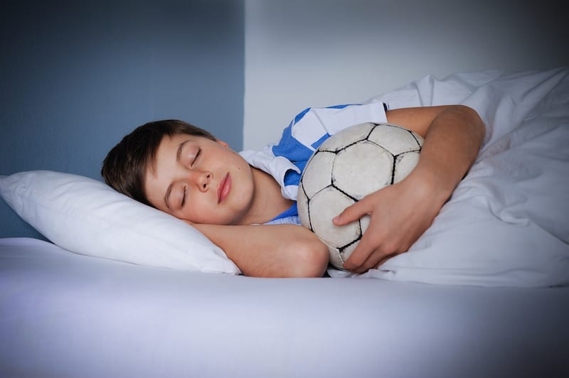 Sleep, Athletic Performance, and Recovery A Young boy asleep with Soccer ball